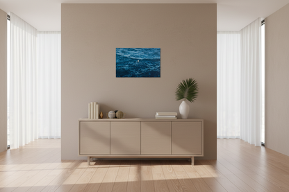 Framed artwork of a blue ocean scene on a wall above a cabinet with decorative items.